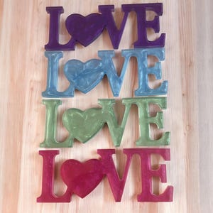 May include: Four sets of the word "LOVE" spelled out in large, colorful letters with a heart in the center of each set. The letters are purple, blue, green, and red.