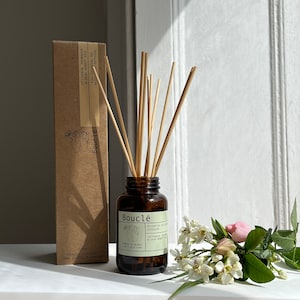 May include: A brown glass bottle with a label that reads "Boucl&eacute; Essential Oil Diffuser" with a bouquet of white flowers and a brown cardboard box with the same text on the label.