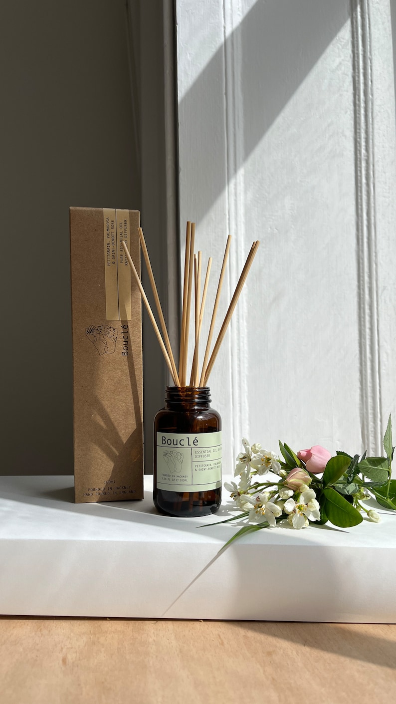 May include: A brown glass bottle with a label that reads "Boucl&eacute; Essential Oil Diffuser" with a bouquet of white flowers and a brown cardboard box with the same text on the label.