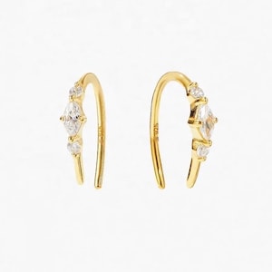 Puede incluir: Un par de pendientes de aro de oro con una piedra transparente de forma marquesa y dos piedras redondas transparentes más pequeñas en cada pendiente.