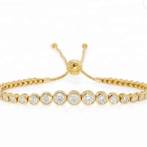 May include: A gold bracelet featuring a line of round, clear stones. The bracelet has an adjustable clasp.