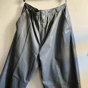 May include: Gray leather pants with a high waist and a button closure. The pants have pockets on the sides and back.