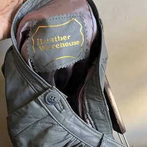 May include: Gray leather jacket with a label that reads "The Leather Warehouse" inside the collar.