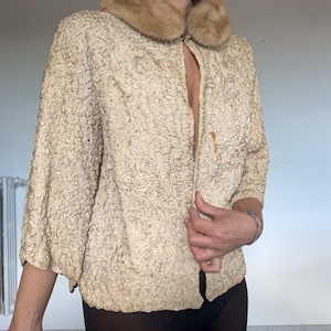 May include: A cream-colored, textured jacket with a brown fur collar. The jacket has a button closure and long sleeves.
