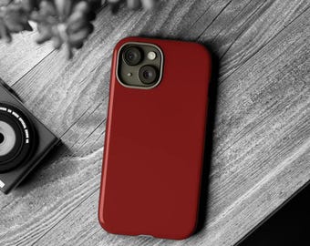 May include: A solid deep red smartphone case featuring a dual-lens camera cutout with a metallic grey border. The case has a smooth, matte finish and covers the back of the device, providing a clean, uniform appearance for the mobile phone.