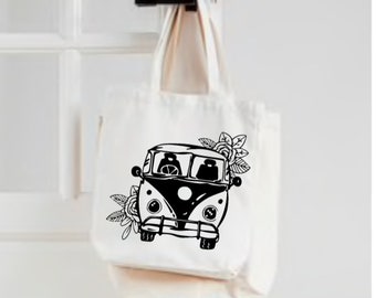 May include: Cream-coloured canvas tote bag with a black and white graphic of a vintage van and floral details. The bag is suspended from a black door handle. The design is a simple, yet stylish, illustration.