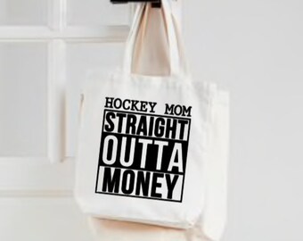 May include: A cream canvas tote bag with the text "HOCKEY MOM STRAIGHT OUTTA MONEY" in black. The bag is suspended from a black door handle. The background is a white door. The tote bag has two handles.