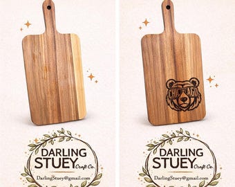 May include: Handcrafted wooden cutting board with a handle. The board is made of light brown wood and features the text "HANDCRAFTED WOODEN CUTTING BOARD". The second board has a bear graphic with the text "CHICAGO".