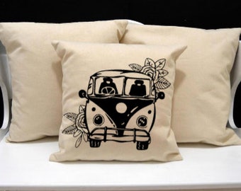 May include: Three cream-coloured square cushions. The central cushion has a black and white illustration of a classic van with floral details. The cushions are made of a soft material, ideal for adding comfort and style to a living space.