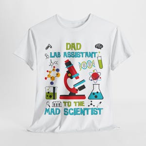 May include: White t-shirt with a science-themed graphic. The design includes a red microscope, molecular structures, and the text "DAD LAB ASSISTANT TO THE MAD SCIENTIST" in green and blue.