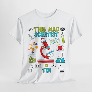 May include: White t-shirt with a colorful science-themed graphic. The design includes a red microscope, molecular structures, and the text "THIS MAD SCIENTIST IS TEN" in green and blue.