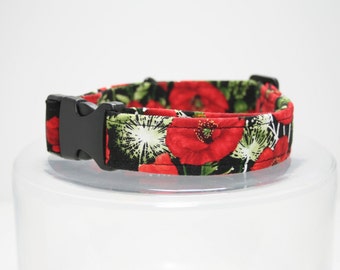 May include: A dog collar with a black plastic buckle. The collar features a floral pattern of red poppies, green leaves, and white accents on a black background. The collar is made of fabric.