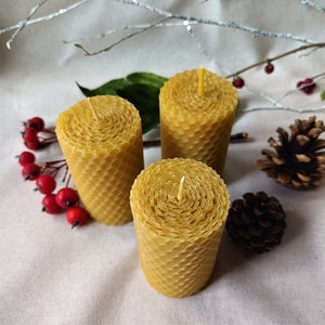 Puede incluir: Tres velas de cera de abeja amarilla con un patr&oacute;n de panal. Las velas est&aacute;n dispuestas en forma triangular sobre una superficie blanca.