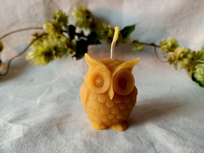 May include: A small, yellow beeswax candle shaped like an owl. The owl has detailed features, including eyes, beak, and feathers.