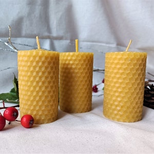 Puede incluir: Tres velas amarillas de cera de abeja con un patr&oacute;n de panal. Las velas est&aacute;n dispuestas en una fila sobre una superficie blanca.