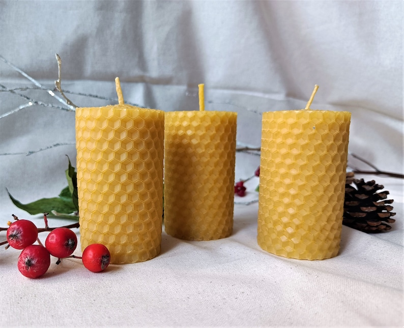 Puede incluir: Tres velas amarillas de cera de abeja con un patr&oacute;n de panal. Las velas est&aacute;n dispuestas en una fila sobre una superficie blanca.