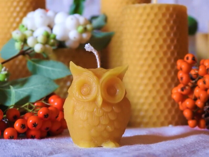 May include: A small, yellow beeswax candle shaped like an owl. The candle has a white wick and is sitting on a white surface.