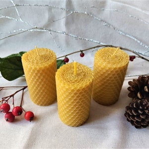 Puede incluir: Tres velas amarillas de cera de abeja con un patr&oacute;n de panal. Las velas est&aacute;n dispuestas en forma triangular sobre una superficie de tela blanca.