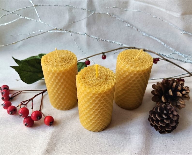 Puede incluir: Tres velas amarillas de cera de abeja con un patr&oacute;n de panal. Las velas est&aacute;n dispuestas en forma triangular sobre una superficie de tela blanca.