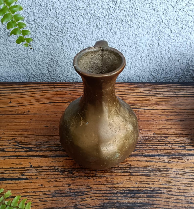 Op de afbeelding: Een messing vaas met een getextureerd oppervlak en een rond lichaam. De vaas heeft een korte, brede hals en een handvat.