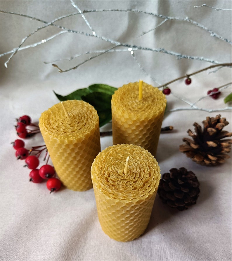 Puede incluir: Tres velas de cera de abeja amarilla con un patr&oacute;n de panal. Las velas est&aacute;n dispuestas en forma triangular sobre una superficie blanca.
