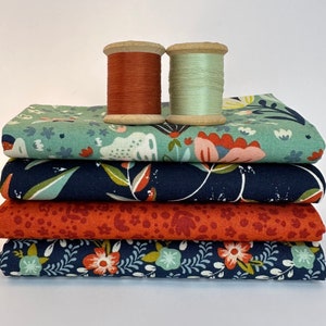 Könnte beinhalten: Ein Stapel aus fünf Stoffquadraten mit Blumenmustern in Blautönen, Grün, Rot und Orange. Zwei Garnrollen, eine orange und eine grüne, liegen oben auf dem Stoff.