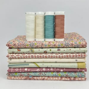 Könnte beinhalten: Ein Stapel gemusterter Stoffe in verschiedenen Farben, gekrönt von vier Garnrollen. Die Stoffe weisen Blumen- und geometrische Designs in Rosa, Grün und Creme auf. Die Garnrollen sind weiß, cremefarben, türkis und braun.