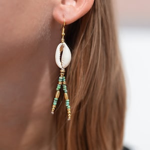 May include: A pair of gold earrings with a white seashell charm and green and gold beads dangling from the bottom.