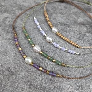 Può includere: Quattro delicate collane con piccole perline e perle. Le collane sono realizzate con perline di diversi colori, tra cui verde, viola e bianco. Le collane sono infilate su un cordoncino marrone.