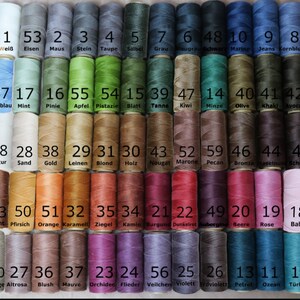 May include: A chart of 60 spools of thread, each with a different colour and number. The spools are arranged in rows of 12. The numbers 1 through 60 are printed on the spools, along with the corresponding colour names in German.