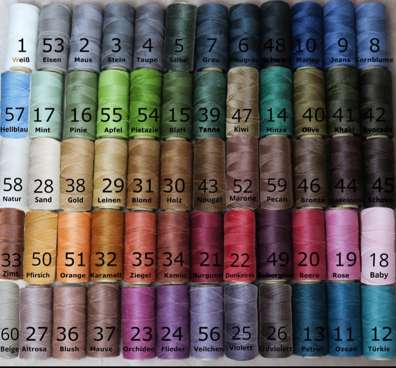 May include: A chart of 60 spools of thread, each with a different colour and number. The spools are arranged in rows of 12. The numbers 1 through 60 are printed on the spools, along with the corresponding colour names in German.
