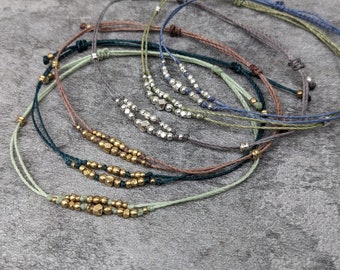 May include: A set of six delicate bracelets with various coloured cords and small beads. The bracelets feature a mix of silver and gold beads.
