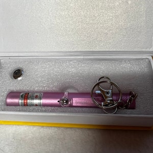May include: A pink laser pointer with a keychain attached. The laser pointer has a warning label that reads "DANGER".