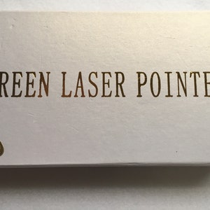 May include: White box with gold lettering that reads "GREEN LASER POINTER".