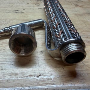 May include: A disassembled metal object with a threaded end, a cylindrical component, and a braided design. The object is silver and copper-colored, and appears to be a part of a larger mechanism or tool.