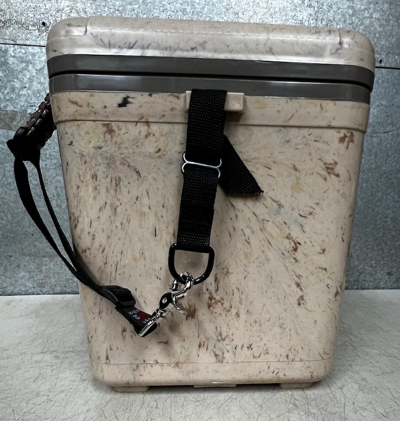 Pode incluir: Uma geleira bege salpicada com uma al&ccedil;a preta e acess&oacute;rios prateados. A geleira tem formato retangular com tampa e uma al&ccedil;a preta para transporte. O exterior apresenta um padr&atilde;o salpicado com tons de castanho e bege.