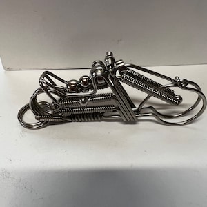 May include: A silver metal motorcycle keychain with a spring design. The motorcycle has a round seat and a spring for the front suspension.