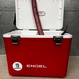 K&ouml;nnte beinhalten: Ein roter Engel-K&uuml;hlbox mit einem wei&szlig;en Deckel und einem wei&szlig;en Etikett mit der Aufschrift "19 Quarts". Die K&uuml;hlbox hat einen wei&szlig;en Griff und einen wei&szlig;en Gurt. Die K&uuml;hlbox ist ge&ouml;ffnet und ein roter Schlauch befindet sich im Inneren.