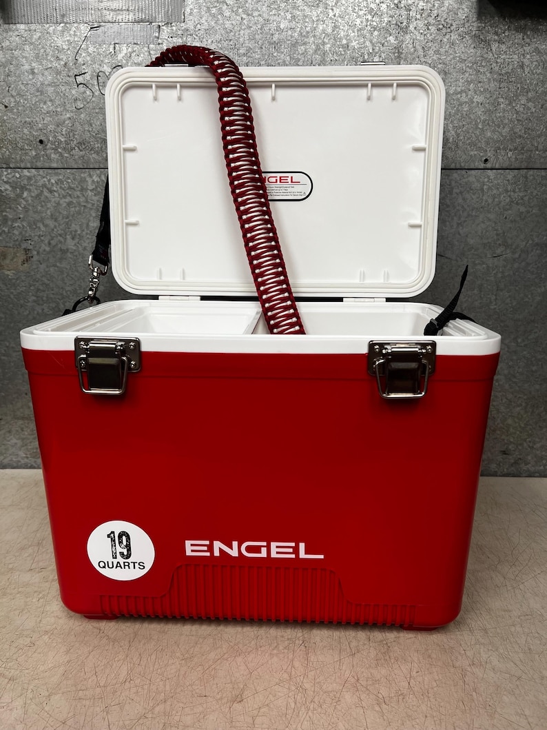 K&ouml;nnte beinhalten: Ein roter Engel-K&uuml;hlbox mit einem wei&szlig;en Deckel und einem wei&szlig;en Etikett mit der Aufschrift "19 Quarts". Die K&uuml;hlbox hat einen wei&szlig;en Griff und einen wei&szlig;en Gurt. Die K&uuml;hlbox ist ge&ouml;ffnet und ein roter Schlauch befindet sich im Inneren.
