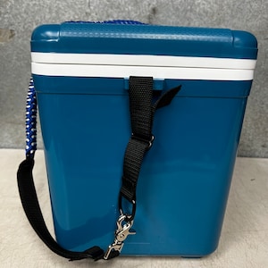 May include: A blue and white cooler with a black strap and a silver hook. The cooler has a textured surface and a white lid.