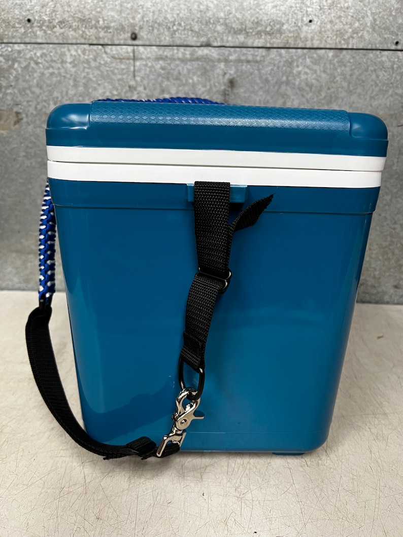 May include: A blue and white cooler with a black strap and a silver hook. The cooler has a textured surface and a white lid.