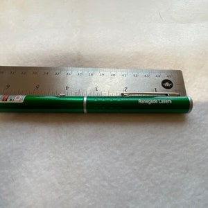 May include: A green laser pointer with a silver end cap and the text "Renegade Lasers" printed on the side. The laser pointer is measured against a ruler.