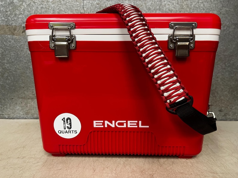 K&ouml;nnte beinhalten: Rote K&uuml;hlbox mit einem wei&szlig;en Streifen und einem schwarzen Gurt. Die K&uuml;hlbox hat einen wei&szlig;en Aufkleber mit der Aufschrift "19 Quarts" und das Wort "ENGEL" ist auf der Vorderseite aufgedruckt.