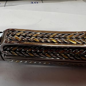 May include: A silver and gold pen with a braided design. The pen has a silver clip and a silver cap.