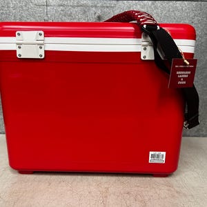 K&ouml;nnte beinhalten: Rote und wei&szlig;e K&uuml;hlbox mit schwarzem Riemen und einem wei&szlig;en Etikett mit der Aufschrift "Exclusive Lager & Pilsner"