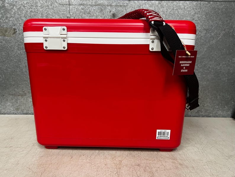 K&ouml;nnte beinhalten: Rote und wei&szlig;e K&uuml;hlbox mit schwarzem Riemen und einem wei&szlig;en Etikett mit der Aufschrift "Exclusive Lager & Pilsner"