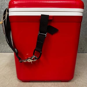 K&ouml;nnte beinhalten: Rote K&uuml;hlbox mit wei&szlig;em Deckel und schwarzem Gurt. Die K&uuml;hlbox hat einen silbernen Verschluss am Gurt.