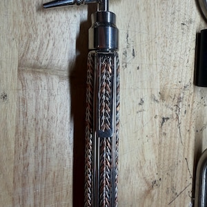 May include: A metal wine bottle opener with a braided copper and silver handle. The opener has a T-shaped design with a pointed tip. The handle is approximately 5 inches long.