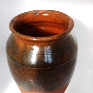May include: A brown and black ceramic pot with a rounded shape and a wide opening. The pot has a glazed finish and is made of earthenware.