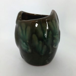 Puede incluir: Un pequeño jarrón de cerámica verde y marrón con una forma orgánica única. El jarrón tiene un acabado brillante y un esmalte moteado.